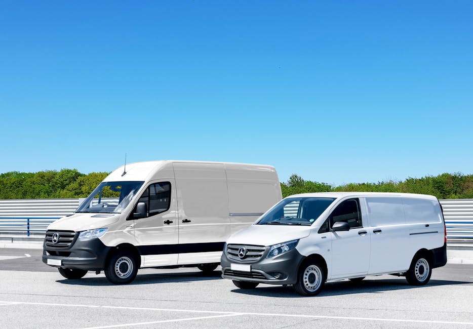 Two white Mercedes-Benz vans parked on a paved road during daytime, with the larger van in the background and the smaller van in the foreground. The vehicles are positioned side by side, with the larger van facing slightly to the left and the smaller van facing directly forward. Both vans are used for house removals and loading processes, with visible sliding side doors closed and no occupants inside. The larger van appears to be a high-roof model, suitable for transporting furniture and packed boxes, while the smaller van is likely used for smaller loads or parcel deliveries. The road surface is clear, with painted lane markings and a barrier fence on the side, beyond which there are lush green trees under a bright blue sky. The setting suggests a relocation or furniture transport scenario, aligned with house moving services such as those offered by Man with Van North Harrow, highlighting professional logistics and vehicle readiness for home relocation tasks.
