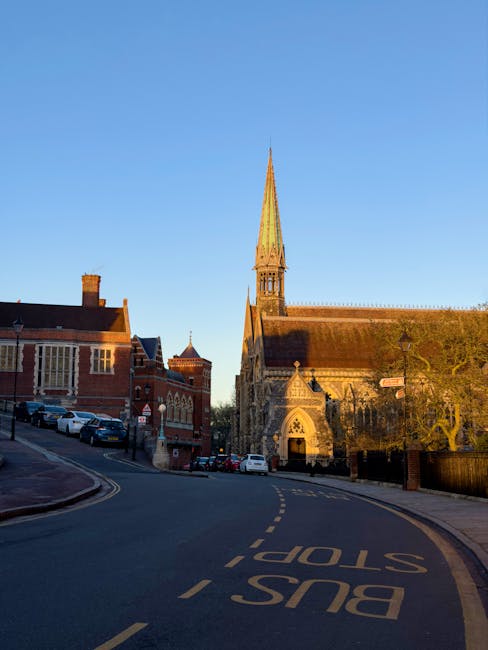 A quiet street scene in North Harrow during the early evening, showing a curved road with a double yellow line along the curb, and a corner area with a stone wall and a blue street lamp post. On the l