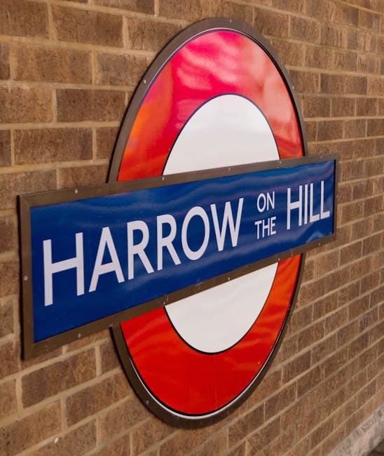 Close-up of a London Underground roundel sign mounted on a brick wall, displaying the name 'Harrow on the Hill' in white capital letters on a blue rectangular background. The sign features a red outer circle with a white center, with the blue nameplate positioned horizontally across the middle. The background consists of a textured brick wall with earthy tones, and the lighting highlights the reflective surface of the sign, suggesting an indoor or sheltered environment. This sign is associated with public transport and the Harrow area, relevant to house removals and moving logistics in North Harrow by Man with Van North Harrow, emphasizing the local transport infrastructure involved in home relocation services.